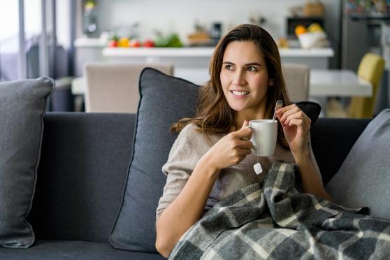 Woman holding a drink cup on the couch for a story on natural ways to ease a cold